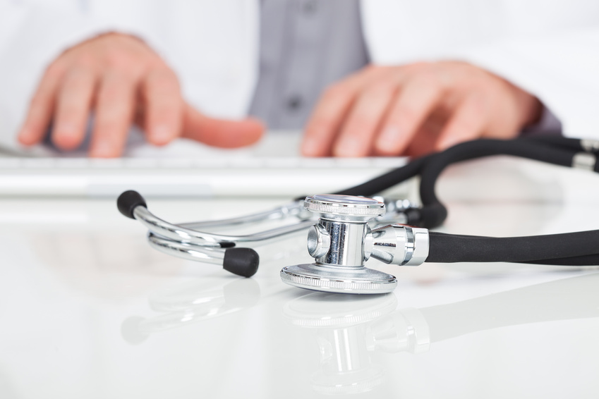 Close-up Of Doctor's Hand Typing On Keyboard In Front Of Stethoscope